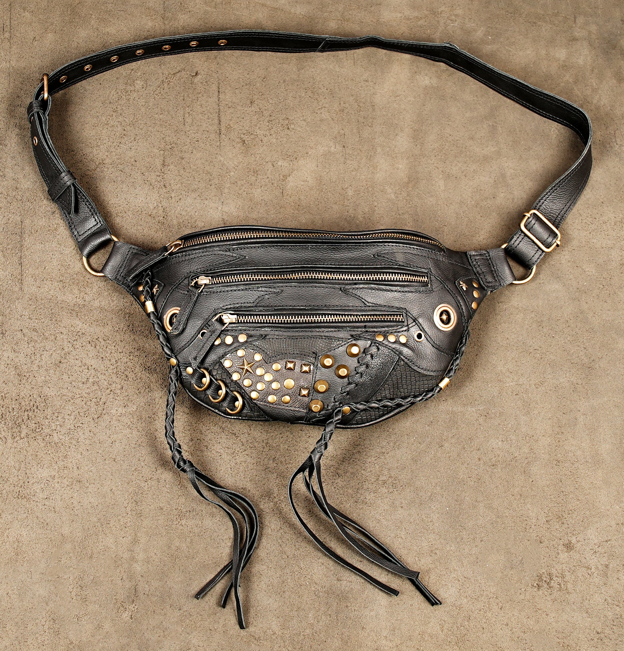Vintage-inspired black leather fanny pack with gold-tone metal studs and braided fringe details.