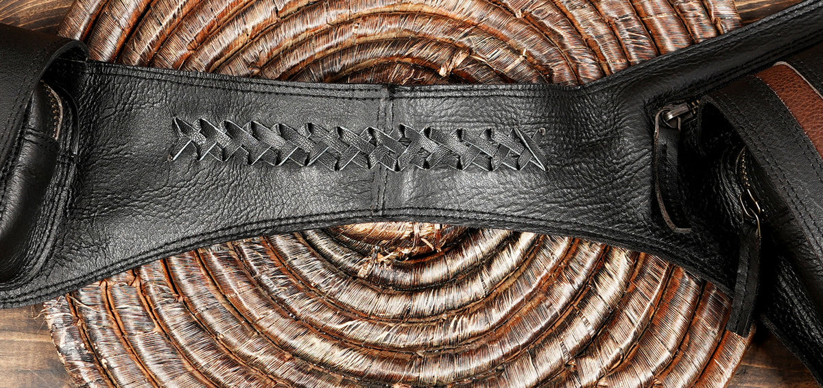 A close-up of a black leather strap with decorative stitched detailing, laid over a woven brown and tan circular mat on a wooden surface.