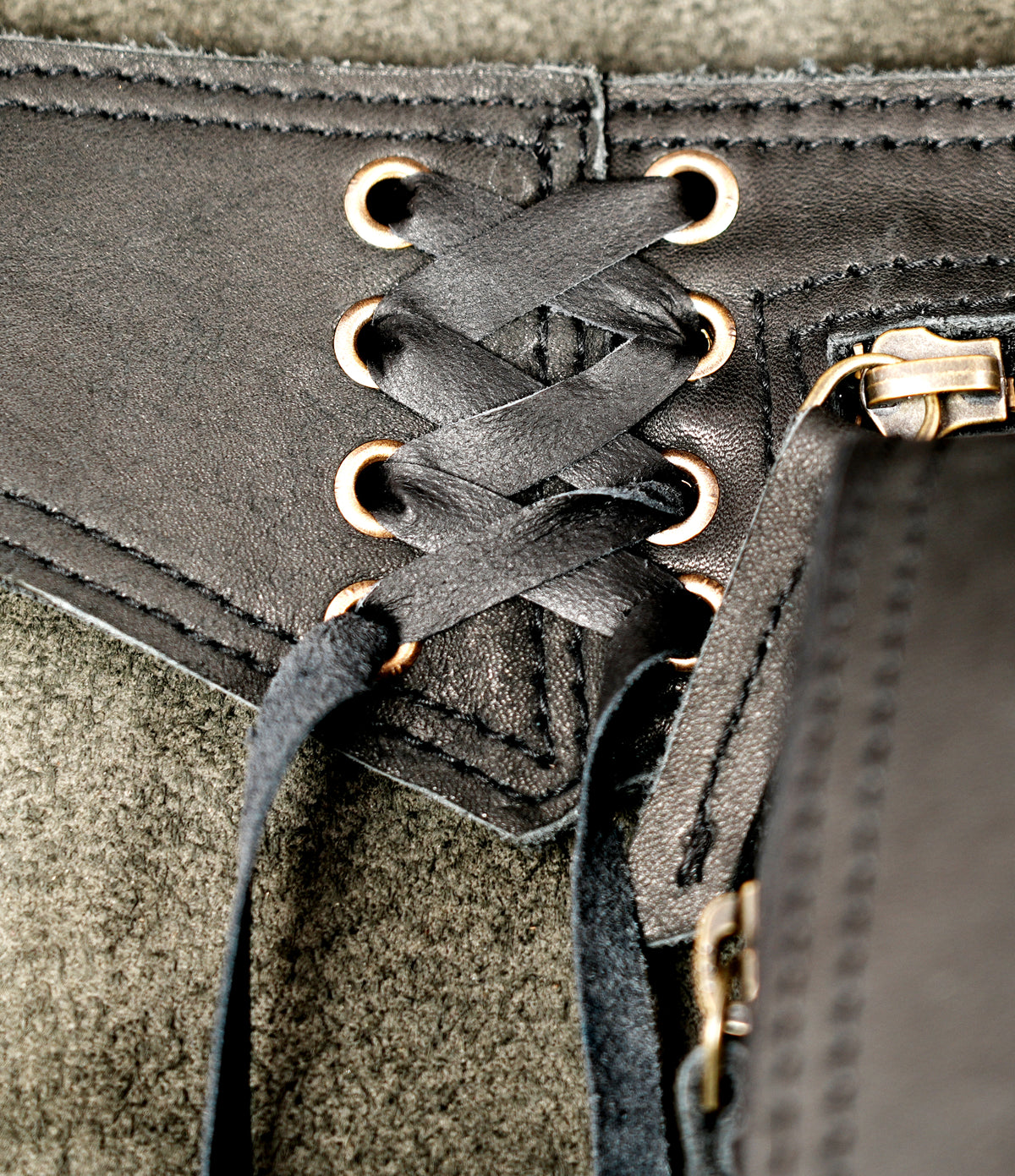 Close-up of a black leather lace-up belt with gold-tone metal eyelets and a zipper closure.