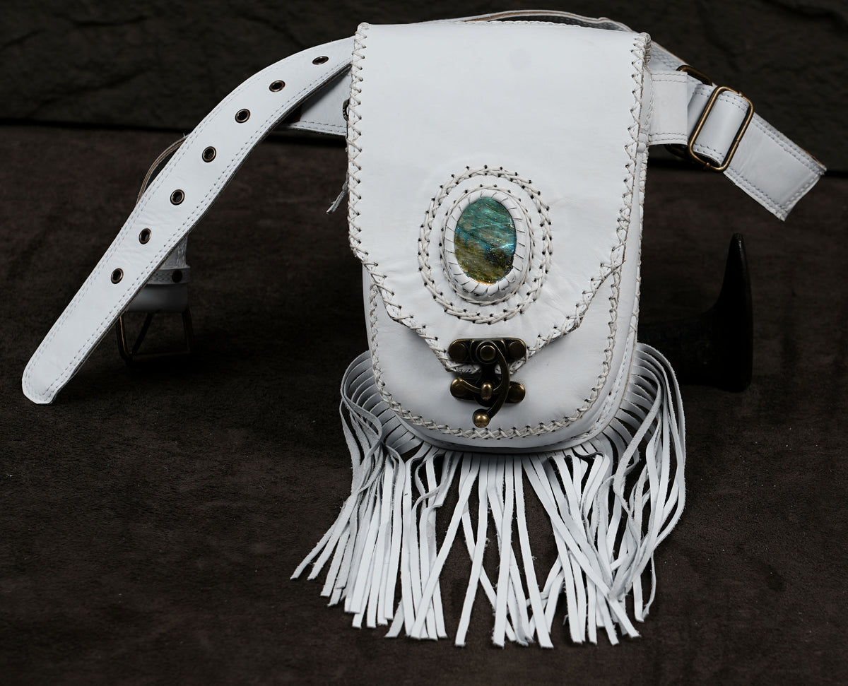 A white leather shoulder bag with fringe detailing, featuring a central oval stone inlay and a decorative metal clasp.