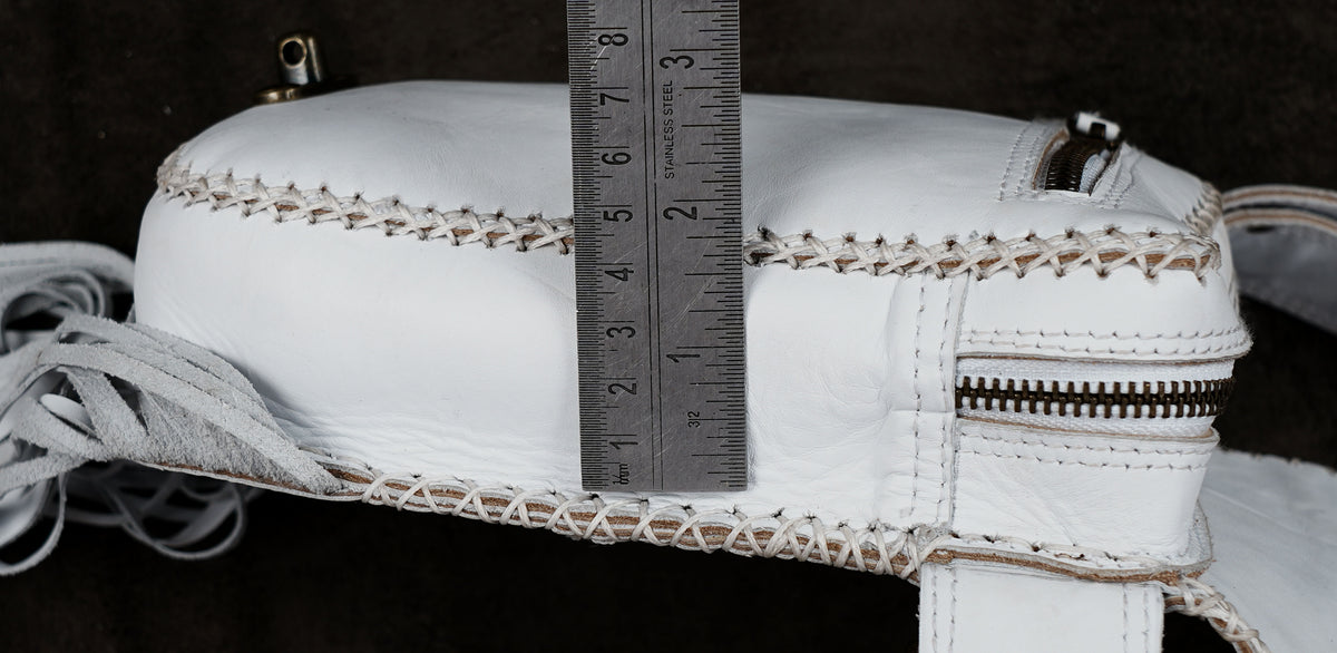 A close-up of a white leather bag or case with visible stitching, a zipper, and a metal ruler standing vertically to show dimensions.
