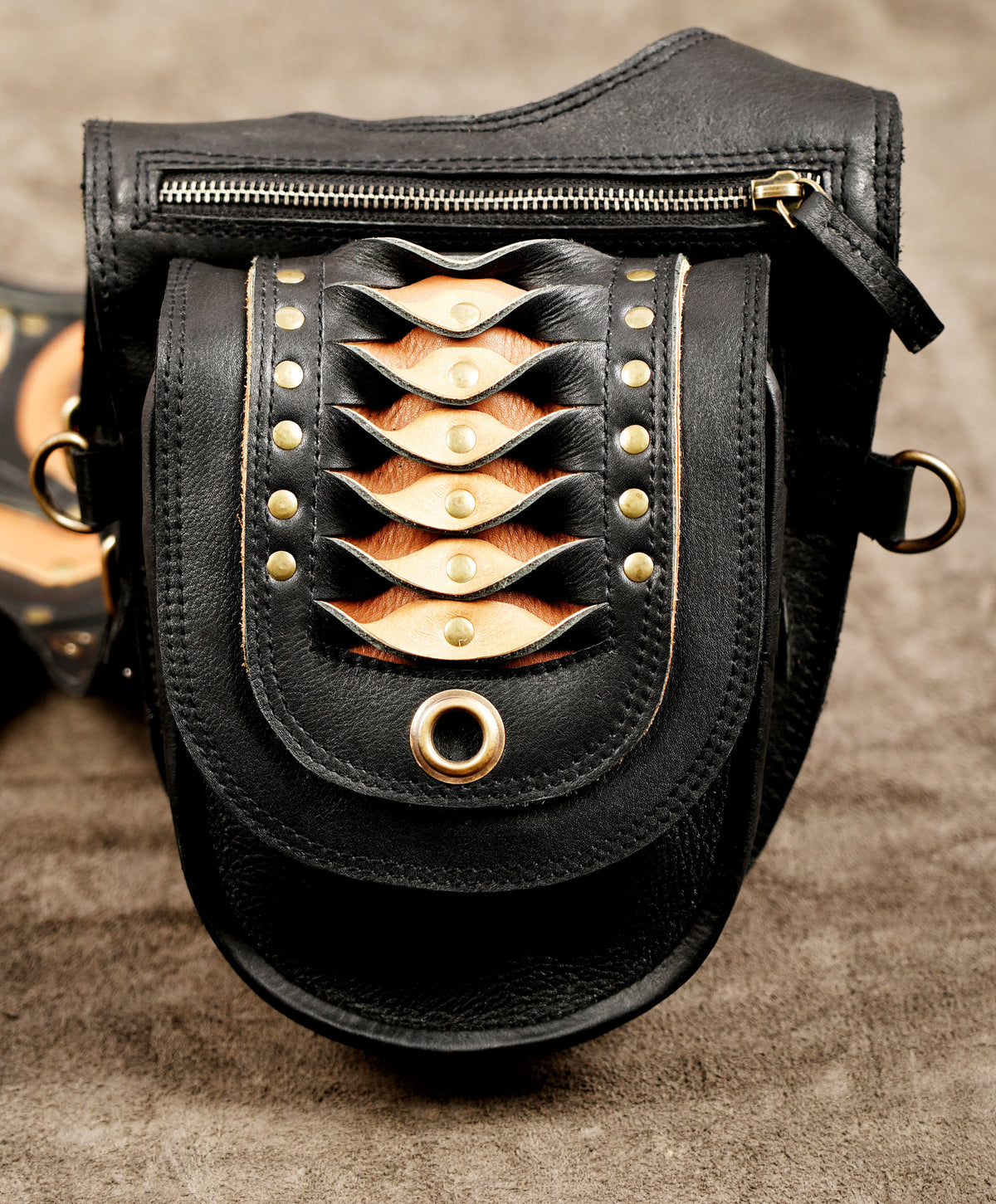 Black leather shoulder holster bag with curved pockets and decorative brass eyelets.