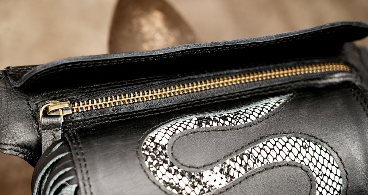 Close-up of a black leather bag with a gold zipper and a snakeskin-patterned accent.