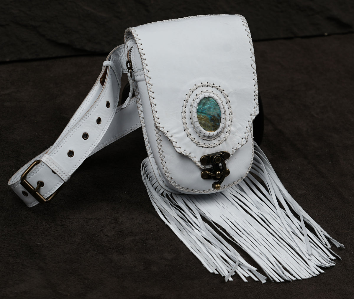 White leather fringe pouch with a flap closure, decorative oval inlay, and matching white shoulder strap.