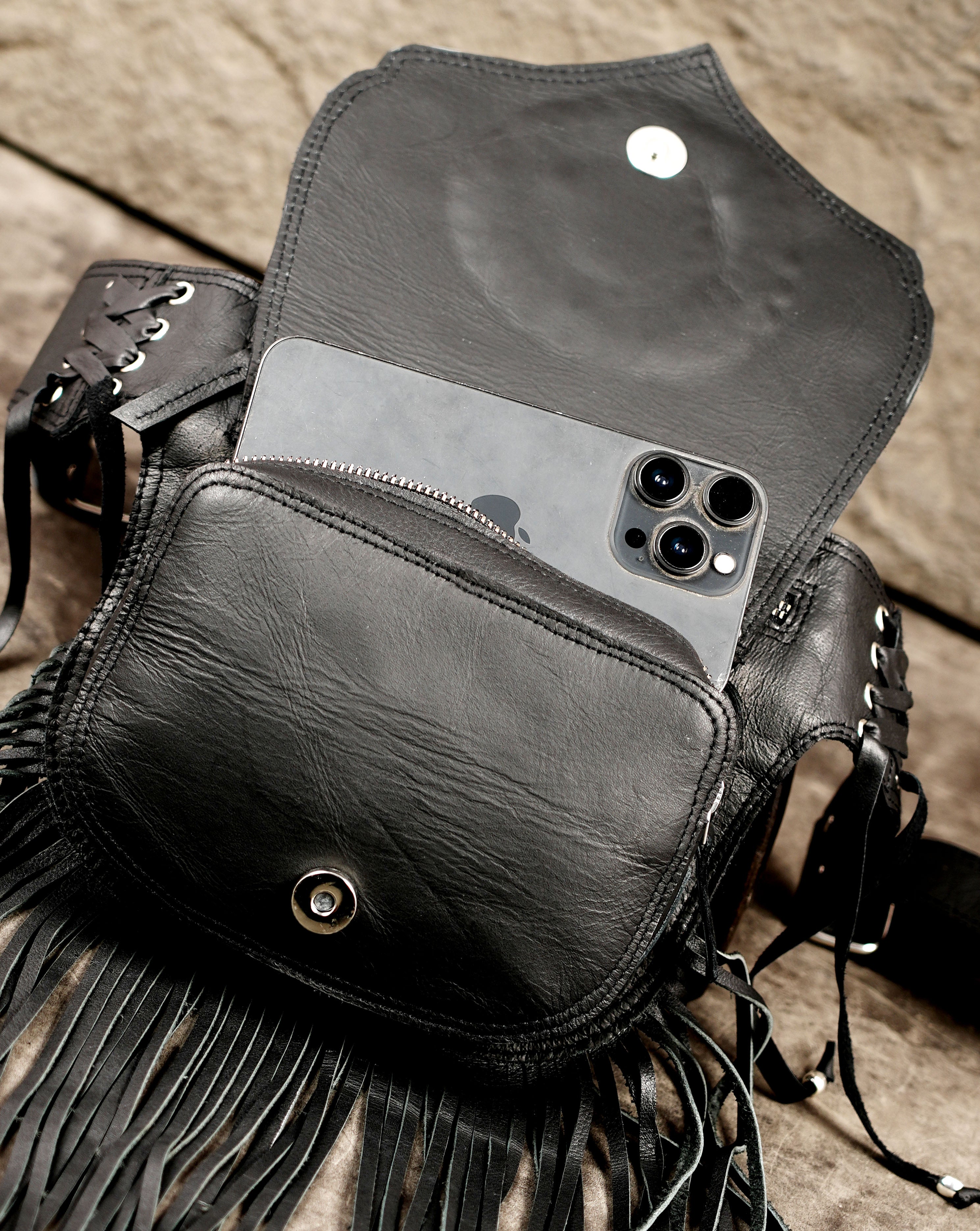 Handcrafted leather waist bag with fringe, close up on stone