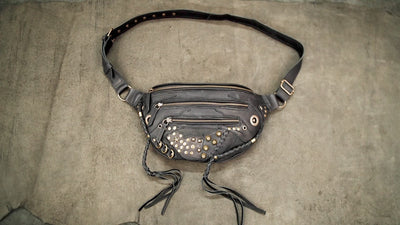 Bohemian style black leather hip holster purse with gold grommets and hanging leather tassels.