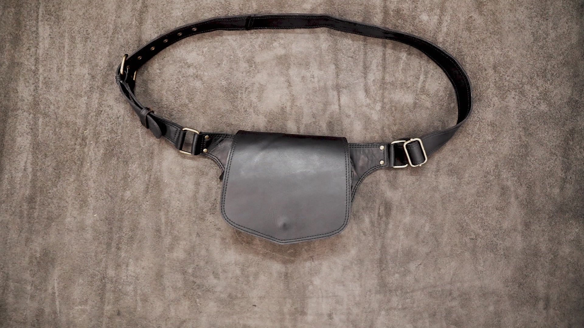 Handcrafted black leather bum bag showing adjustable brass buckle detail.