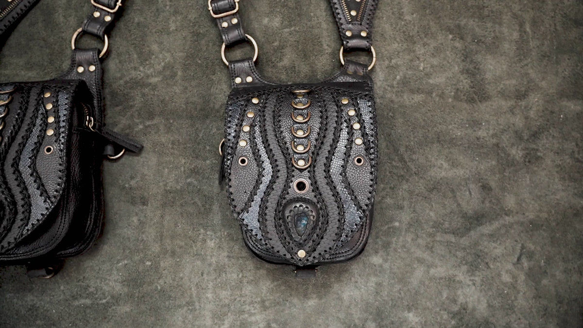 Edgy black leather shoulder holster bag with double utility pouches and metal hardware worn by a model against a grey studio background