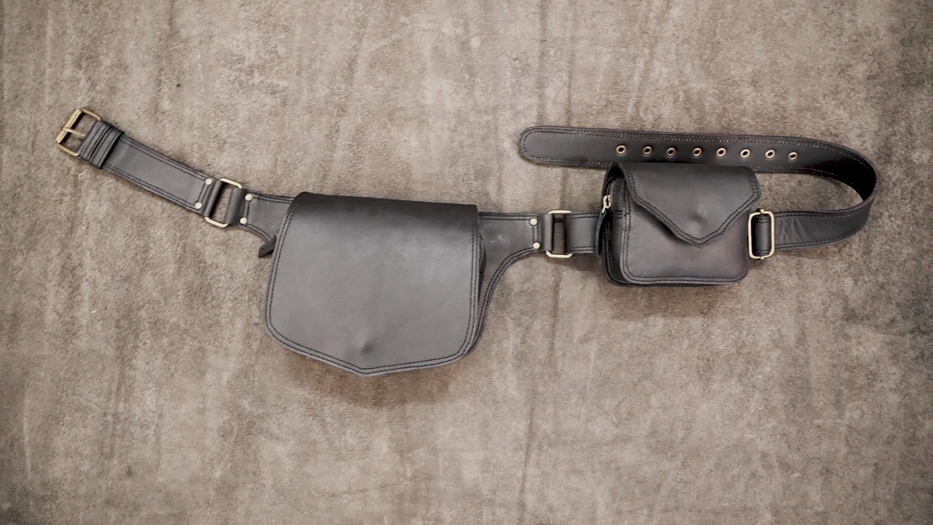 Black leather festival utility belt with dual pouches and brass hardware laid flat on a neutral background   